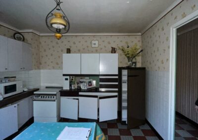Photo avant travaux d'une cuisine ancienne avec papier peint fleuri, carrelage damier et luminaire rétro, projet de rénovation complète à Bignan par Reflets & Design architecte d'intérieur dans le Morbihan